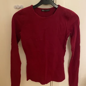 Vinröd långärmad tröja från Zara - Säljer en enkel och stilren vinröd långärmad tröja från Zara i storlek XS. Tröjan har rund halsringning och är gjord i mjuk bomull som sitter skönt mot kroppen. Perfekt att matcha med jeans eller kjol för en clean look.