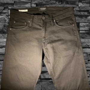 Svarta slim fit jeans Jack & Jones - Svarta jeans från Jack & Jones i modellen Glenn med slim fit-passning. Klassisk femficksdesign, knapp och dragkedja i gylfen. Snyggt stilrena och passar perfekt till sneakers eller boots. Materialet är jeans med en mjuk känsla.