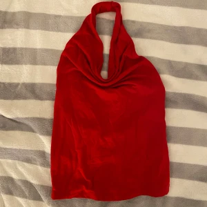 Röd omlott halternecktopp - Snygg röd topp med halterneck och omlott-detalj. Toppen är ärmlös och har en tight passform som framhäver figuren. Tillverkad i ett mjukt, glansigt material som ger en lyxig känsla. Perfekt för dig som vill sticka ut med en enkel men iögonfallande look. ANVÄND 1 GÅNG