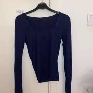Mörkblå långärmad topp Gina Tricot XS - Mörkblå långärmad topp från Gina Tricot i storlek XS. Modellen har rund halsringning, slits vid ärmslut och är figurnära. Perfekt att styla med jeans eller kjol för en enkel och snygg look.
