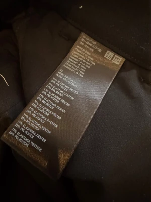 Svarta tapered kostymbyxor med resår - Säljer ett par svarta kostymbyxor med tapered passform och resår i midjan. Byxorna har dragkedja och knappstängning, samt hällor för bälte. Materialet känns mjukt och har en snygg, stilren look. Perfekt för dig som gillar en clean och modern stil.