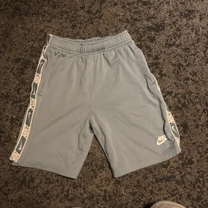 Nike Dri-Fit ljusblå shorts  - Nike Dri-Fit shorts i ljusblått med elastisk midja och vita detaljer längs sidorna med Nike-logga. Sköna och lätta, perfekta för träning eller chill. Materialet är polyester som andas och håller dig torr. Snygg sportig look med normal passform.