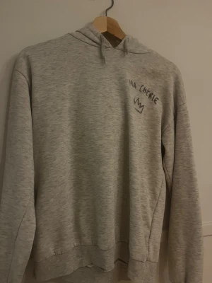 Grå hoodie med Ma Chérie-tryck - Säljer en grå ma cherie tröja dock har den en liten fläck i mitten på tröjan och metall  saken på snörena har åkt av