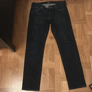 Lee Daren Zip Fly jeans mörkblå W33 L32 - Mörkblå jeans från Lee, modell Daren Zip Fly. Klassisk femficksdesign med raka ben och normal passform. Jeansen har dragkedja i gylfen och brunt Lee-läderpatch bak i midjan. Snygga kontrastsömmar och tillverkade i slitstarkt denimtyg.