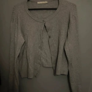 Grå ribbad kofta från 157, storlek L - Säljer en grå ribbad kofta från 157 i storlek L. Koftan har rund hals, långa ärmar och knappar framtill. Den är stickad och har en loose passform som gör den chill och enkel att matcha med jeans eller kjol.