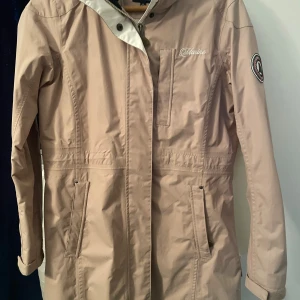 Beige vindjacka från Marine Scandinavian - Snygg beige vindjacka från Marine Scandinavian Sportswear med dragkedja och tryckknappar framtill. Jackan har praktiska fickor, lång ärm och coolt märke på ena armen. Perfekt för blåsiga dagar och har en stilren look med diskreta detaljer.