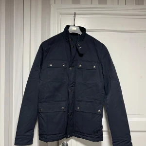 Mörkblå parkajacka från Firetrap Storlek S - Snygg mörkblå parkajacka från Firetrap med fyra stora fickor framtill och silverfärgade knappar. Jackan har hög krage med knäppning och dragkedja, helt ny aldrig använd. Storlek S