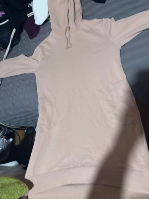 Beige hoodieklänning med huva - Säljer en beige hoodieklänning från H&M i storlek 38. Klänningen har lång ärm, huva med snörning och praktiska fickor på sidorna. Mjuk och skön i bomullsmaterial, perfekt för chill dagar. Enkel och stilren design som är lätt att matcha med sneakers.