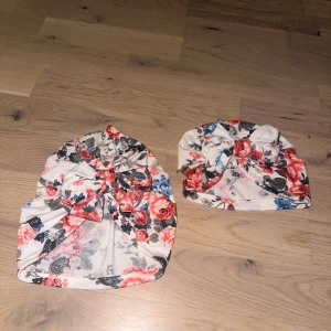 Blommiga turbanmössor med rosett - Två mjuka turbanmössor i beige med blommigt mönster i rött, blått och svart. Framtill sitter en snygg rosett som ger extra stilpoäng. Perfekt för dig som vill ha en unik och färgglad look. Passar både till chill och när du vill sticka ut lite extra. Ena är för bebis från 3-6 månader + och den andra turbanen är för större flicka/mamma onesize 