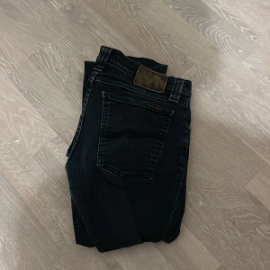 Svarta jeans från Nudie Jeans Co - Säljer ett par svarta jeans från Nudie Jeans Co med klassisk femficksdesign och snygga kontrastsömmar. Jeansen har rak passform och är tillverkade i slitstarkt bomullsjeansmaterial. Perfekta för dig som gillar stilrena och tidlösa jeans.