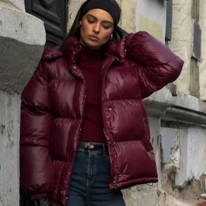 Vinröd pufferjacka med huva - Säljer en vinröd pufferjacka med huva och dragkedja. Jackan har en oversized passform, quiltad design och är tillverkad i glansig polyester. Perfekt för kalla dagar och har långa ärmar samt praktiska fickor. Styla med jeans och boots för en cool look. Säljer pga jag skulle önskat den lite längre men eftersom jag är rätt lång så ser den nog perfekt ut på någon kortare än mig.☺️Bilder tagna från deras hemsida. Om önskas kan jag skicka på mig själv. Öppen för förhandling vid snabbbaffär❤️