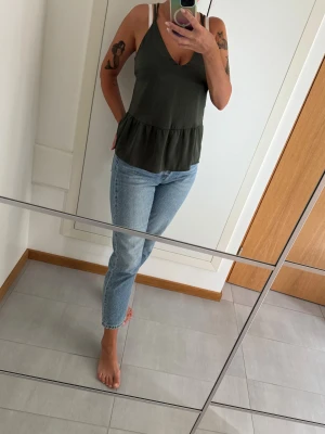 Mörkgrön linnetopp från H&M Divided - Supersnygg mörkgrön linnetopp från H&M Divided i storlek 36. Toppen har tunna dubbla axelband, v-ringning och volang nedtill. Tillverkad i mjuk polyester som ger ett lätt och luftigt fall. Mörkgrönt/smaragdgrönt linne i siden imitation med smala korslagda axelband och volangkant (peplumtopp). Perfekt till tex julfest / nyår. 