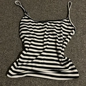 Svartvit randig bikiniöverdel - Snygg bikiniöverdel med smala axelband och klassiskt svartvitt randigt mönster. Materialet är mjukt och stretchigt, perfekt för strandhäng eller poolparty. Passformen är normal och toppen har en enkel, stilren design som är lätt att matcha med andra bikinidelar. Passar XS men även S