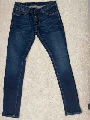 Mörkblå jeans från Nudie - Snygga mörkblå jeans från Nudie Jeans med klassisk femficksdesign och kontrastsömmar. Jeansen är i extremt bra skick och i storlek W32, L34. Pris går att diskutera vid snabb affär!