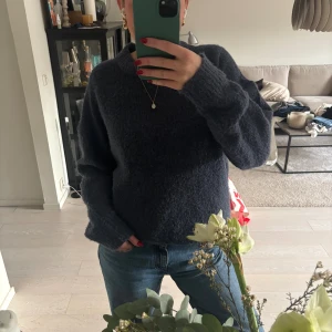 Mörkblå stickad tröja från 157 - Mysig mörkblå stickad tröja från 157 med rund halsringning och lång ärm. Tröjan har en fluffig och grovstickad känsla som gör den perfekt för kyligare dagar. Enkel och stilren modell som är lätt att matcha med jeans eller kjol.