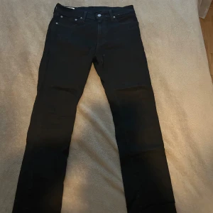 Svarta Levi's jeans  - Svarta jeans från Levi's modell 511 med klassisk femficksdesign och smal passform. Byxorna har raka ben och är tillverkade i mjukt jeanstyg med knapp och dragkedja framtill. Perfekta för dig som gillar stilrena och tidlösa jeans.