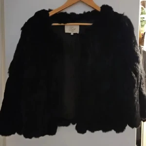 Svart pälsjacka från Furst - Säljer en svart pälsjacka från Furst med croppad passform. Jackan har långärmade ärmar och en fluffig, mjuk yta som ger en lyxig vibe. Perfekt för dig som vill sticka ut med en cool och trendig look.