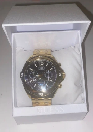 Guess guldig klocka med svart urtavla - Säljer en snygg klocka från Guess med guldig länk och svart urtavla. Klockan har flera små urtavlor, tydliga vita markeringar och robust design. Perfekt accessoar för dig som vill sticka ut med stilren och modern look.