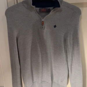 Grå merinoulltröja Morris half zip - Snygg grå långärmad tröja från Morris i 100% merinoull med half zip och liten broderad logga på bröstet. Tröjan har ribbade muddar och en stilren, klassisk look som funkar till jeans eller chinos. Perfekt för dig som gillar enkel och clean stil.