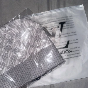 Grå rutig mössa - Snygg grå mössa med klassiskt rutigt mönster och ribbad kant. Märkesplakett i metall framtill ger en lyxig touch. Perfekt accessoar för dig som gillar  streetstyle och vill sticka ut.