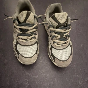 Asics Gel Nyc - Säljer ett par snygga Asics sneakers i grått och vitt med coola detaljer, extra snöret (den gråa) kan tas bort om det önskas, pris kan diskuteras vid snabba affärer!!!!!