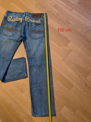 Blå Replay Brand jeans med broderi - Säljer ett par blå jeans från Replay Brand med snyggt broderad logga över bakfickorna och coola detaljer på fickorna. Klassisk femficksmodell i jeansmaterial med raka ben och normal passform. Perfekt för dig som gillar streetstyle och vill sticka ut.