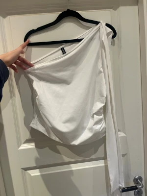 Fin festtopp - säljer denna vita one shoulder toppen som är perfekt till fest. Helt oanvänd och passar mig som vanligtvis är S/M. Axelbandet går att göra lite vad man vill med, antingen knyta till en rosett, snurra runt halsen eller låta det hänga som det är🤩