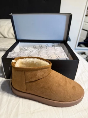Bruna boots från 2MOONS med foder - Mysiga bruna boots från 2MOONS med rund tå och platt sula. Utsidan är i mjuk mocka och insidan har fluffigt ljust foder som håller fötterna varma. Perfekt för kalla dagar och chill outfits. Snygg enkel design med låg skaft och bekväm passform.