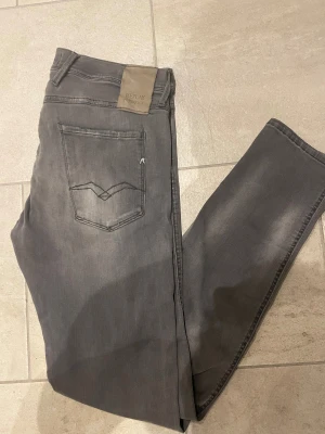 Replay anbass grå jeans W33/L32 - Säljer ett par grå Replay anbass jeans med snyggt tvättad look och klassiska fem fickor. Jeansen har raka ben och normal passform, med Replay-logga på bakfickan och patch i midjan. Perfekta för dig som vill ha bekväma och stilrena jeans.