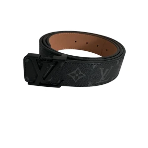 Svart Louis Vuitton skärp i skinn - Snyggt svart skärp från Louis Vuitton med klassiskt monogrammönster och stor LV-logga i matt svart metall. Bältet är gjort i exklusivt skinn och har en stilren, bred design som ger en lyxig känsla till outfiten.