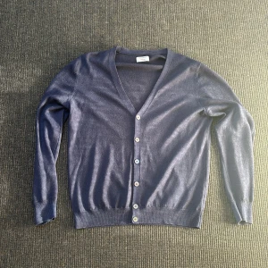 Mörkblå kofta från Gran Sasso - Mörkblå stickad kashmir kofta från Gran Sasso Vintage, tillverkad i Italien. Klassisk v-ringad modell med knappar framtill och långa ärmar. Tunn och mjuk, perfekt för lager-på-lager. Stilren och enkel design som funkar till det mesta. Första bilden med 3 små hål är på vänster armen, andra bilden med ett hål är på höger armen. Annars jätte fint skick! Hör av er vid funderingar! 