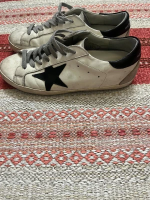 Golden Goose vita sneakers med svart stjärna - Golden Goose sneakers skick är 8/10 dom är använda men försiktigt dom är dock lite smutsiga så behöver en tvätt annars väldigt snygga skor storlek är 41 men kan passa 42