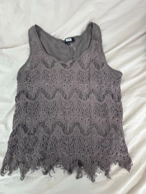 Grå spetsig linnetopp från Bik Bok - Säljer en grå linnetopp från Bik Bok med snygg spets och vågigt mönster. Toppen är ärmlös och har en fransig kant nedtill som ger en cool touch. Perfekt för dig som gillar detaljer och vill sticka ut lite extra.