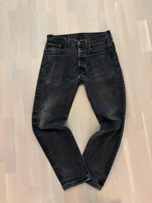 Vintage Levi's 501 - Svarta Levi's 501 jeans med klassisk femficksdesign och knappgylf. Jeansen har en rak passform och är tillverkade i slitstarkt denim med snygga tvättade detaljer. Perfekta för dig som gillar en tidlös och cool look.