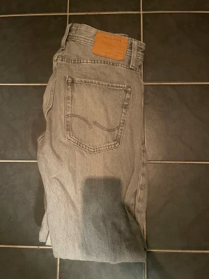 Grå jeans från Jack & Jones - Säljer ett par grå jeans från Jack & Jones med klassisk femficksdesign och rak passform. Jeansen har en snygg, neutral grå färg och är tillverkade i slitstarkt bomullsmaterial. Perfekt för dig som gillar enkel och stilren look.