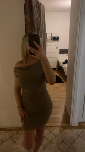 Beige offshoulder kort klänning - Säljer en beige, figurnära kort klänning med offshoulder-design. Klänningen har en snygg draperad halsringning och är tillverkad i ett stretchigt material som sitter tight och framhäver formerna. Perfekt för dig som gillar stilrena och enkla plagg med modern touch.