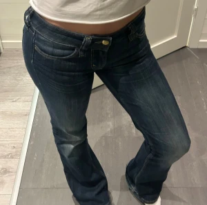 Bootcut jeans från Cheap Monday - Mörkblå bootcut jeans från Cheap Monday med klassisk femficksdesign och snygga slitningar framtill. Låg midja och coolt orange logopatch bak. Jeansen är i stretchigt denim och har en figurnära passform upptill som går ut i ett bootcut vid bensluten.