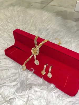 Glittrig guldväst med strassdetaljer - Säljer en glittrig väst i guld med strassdetaljer som ger en lyxig vibe. Västen har ett unikt mönster med gnistrande stenar och en snygg v-ringad form. Perfekt för dig som vill sticka ut och addera extra bling till din outfit. Lådan är inte med