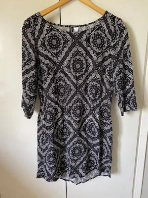 Svartvit mönstrad klänning  - Svartvit klänning med snyggt paisleyinspirerat mönster. Modellen har trekvartsärm och rund halsringning. Perfekt för dig som gillar grafiska prints och vill ha en bekväm, stilren look.