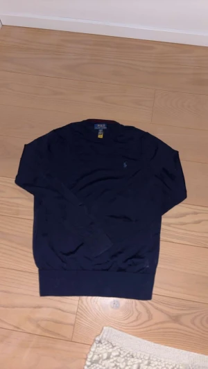 Marinblå Ralph lauren stickad tröja - Fin marinblå stickad Ralph lauren tröja i bra skick. Jag säljer för den har blivit för liten. Storleken är xl barn storlek men passar xs lika bra. Perfekt för den mindre som vill ha en asfet tröja som passar till allt året om! Original pris runt 1440 kr