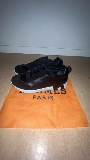  Svarta sneakers - Snygga svarta sneakers med vit, räfflad sula och ovandel i både skinn och mocka. Skorna har snörning och en stilren design som passar perfekt till streetwear. Kommer med dustbag i orange. St 42 men kan passa 43 också, helt nya och för små för mig!