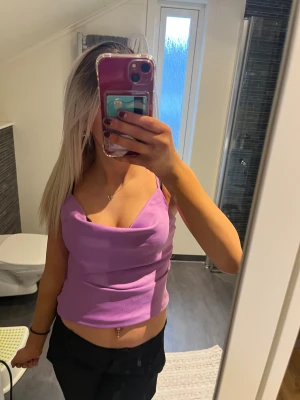 Lila linnetopp från Gina Tricot - Säljer en snygg lila linnetopp från Gina Tricot i storlek 32. Toppen har tunna axelband och en draperad halsringning som ger en chill och trendig vibe. Materialet är mjukt och har en lätt glansig finish som känns lyxig mot huden. Perfekt att styla med jeans eller kjol.