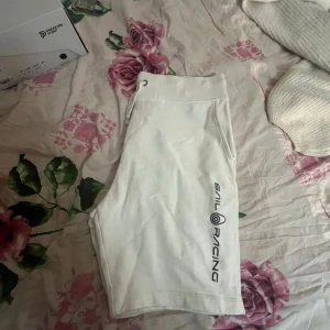 Vita Sail Racing shorts med snörning - (Sail Racing)Fräscha vita shorts från Sail Racing med snyggt tryck längs benet. Modellen har midwaist passform och praktisk snörning i midjan. Tillverkade i mjuk bomull, perfekta för chill dagar eller sportiga aktiviteter. Klassisk look med fickor på sidorna.