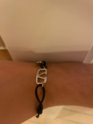 Svart armband från Valentino - Stilrent armband från Valentino. Armbandet har en enkel och modern design med justerbar snörning och detaljer i metall. Perfekt för dig som vill ha en exklusiv touch på din outfit.