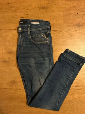 Replay Anbass slim fit jeans blå - Snygga blå Replay Anbass jeans i slim fit med klassisk femficksdesign och diskreta slitningar. Jeansen har normal midja och är tillverkade i mjukt denim med Replay-logga på fickan. Perfekta för dig som gillar en smalare passform och stilren look.