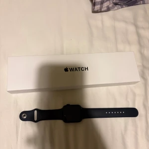 Apple Watch SE (2nd Gen) 44 mm - Säljer en svart Apple Watch med fyrkantig urtavla och mjukt silikonarmband. Klockan kommer med originalförpackning. Priset går att diskutera