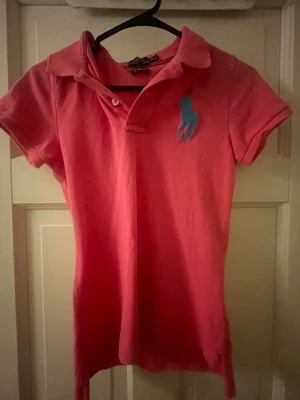 Rosa pikétröja Polo Ralph Lauren  - Säljer en rosa pikétröja från Polo Ralph Lauren. Tröjan har korta ärmar, klassisk krage och blå logga broderad på bröstet. Pris kan diskuteras💕