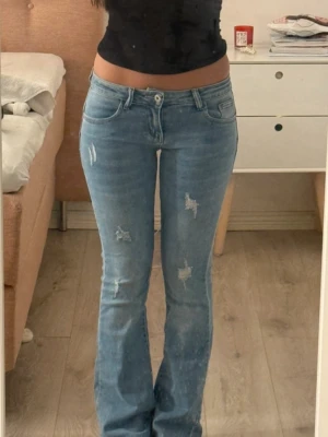 Slitna ljusblåa jeans med slitningar  - Säljer ett par ljusblå lågmidjade bootcut jeans med slitningar. Använda men i väldigt väldigt bra skick. Är i storlek XS och jag är 167 lång och de är långa på mig. Sitter så så snyggt på!