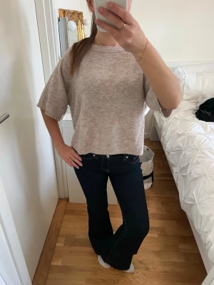 Beige kortärmad stickad tröja - Mysig beige stickad tröja med korta, vida ärmar och boxy passform. Tröjan har rund halsringning och är tillverkad i ett mjukt, melerat material som ger en avslappnad look. Perfekt att matcha med jeans eller kjol.