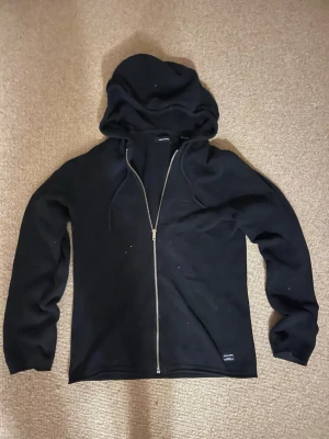 Svart zip hoodie med huva  - En stilren full zip med luva. Perfekt för en avslappnad look och enkel att matcha med andra plagg. Hör av dig vid minsta fundering
